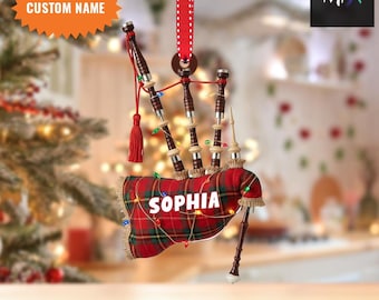 May include: A bagpipe-shaped Christmas ornament with a red and green tartan pattern. The name "SOPHIA" is displayed on the bag. The ornament is decorated with fairy lights and a red tassel, suspended by a red and white polka dot ribbon.