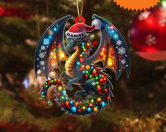 May include: A dragon-shaped Christmas ornament with a Santa hat and the name "Daniel". The dragon is decorated with colorful lights and snowflakes. The ornament has a gold string for hanging and the text "2D FLAT ITEM".