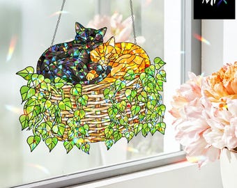 Puede incluir: Colgante de ventana de vidrieras con dos gatos en una cesta de mimbre con hojas verdes. Los gatos son negros y naranjas, y la cesta es marrón. La pieza cuelga de una cadena.