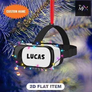May include: A black and white VR headset Christmas ornament with the name "LUCAS" on the front. The ornament is decorated with colorful lights and a red ribbon for hanging. Text on the ornament reads "CUSTOM NAME" and "2D FLAT ITEM".