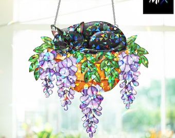 Puede incluir: Adorno decorativo colgante de gato. El gato negro está durmiendo en una cesta de flores de glicina moradas y hojas verdes. El adorno está suspendido por una cadena plateada. El logotipo de Mix está en la esquina superior derecha.