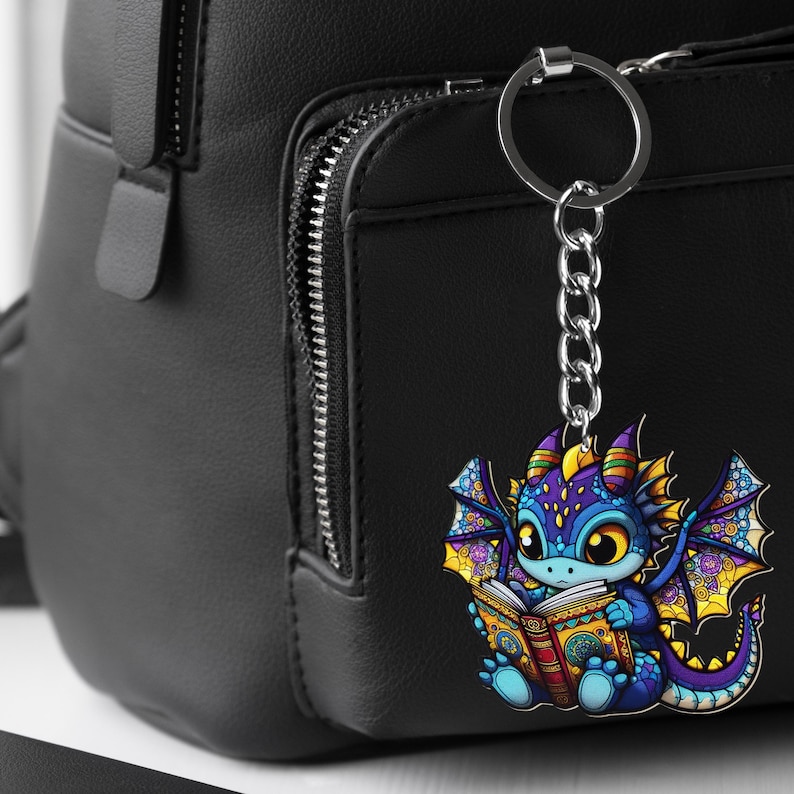 May include: A colorful dragon keychain with a silver chain and ring. The dragon is blue, purple, and yellow, reading a book with gold accents. The keychain is hanging on a black backpack.