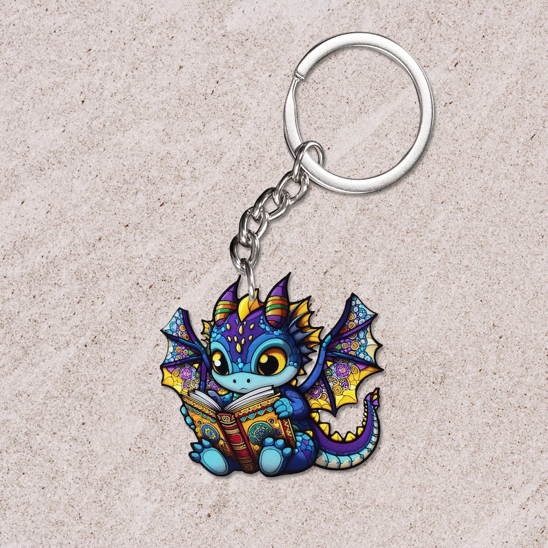 May include: A colorful dragon keychain with a silver chain and ring. The dragon is depicted reading a book, with blue, purple, yellow, and orange hues. The dragon has large eyes and detailed wings. The keychain is a fantasy-themed accessory.