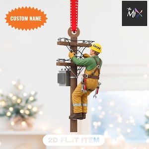 Könnte beinhalten: Ein Weihnachtsschmuck, der einen Elektriker bei der Arbeit an einem Strommast zeigt. Die Figur trägt einen gelben Helm mit der Aufschrift "LUCAS", ein grünes Hemd und gelbe Overalls. Der Schmuck hat ein rot-weiß gepunktetes Band zum Aufhängen. Der Text "CUSTOM NAME" befindet sich oben links.