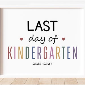 May include: A white framed sign featuring the black text LAST day of and the word KINDERGARTEN in multicolored letters. Two small red hearts flank the word day. The text 2026-2027 appears in black at the bottom of the white rectangular print.