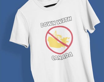 Puede incluir: Camiseta blanca con el texto "DOWN WITH CANADA" sobre un mapa amarillo de Canadá dentro de un círculo rojo con una línea roja que lo atraviesa. La camiseta está colgada en una percha de madera.