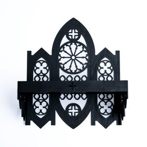 Peut inclure: &Eacute;tag&egrave;re murale en bois noir avec un design de fen&ecirc;tre de cath&eacute;drale gothique. L'&eacute;tag&egrave;re pr&eacute;sente une section centrale arqu&eacute;e avec un motif circulaire, flanqu&eacute;e de petites fen&ecirc;tres cintr&eacute;es. Sur fond blanc.