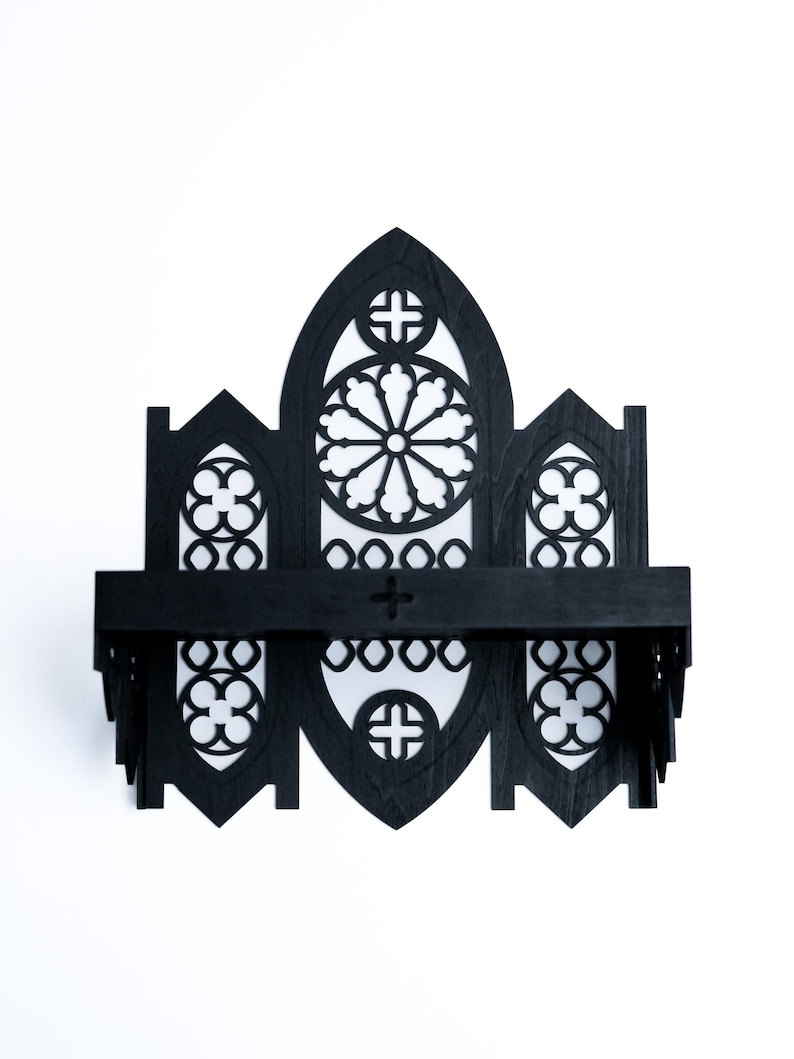 Peut inclure: &Eacute;tag&egrave;re murale en bois noir avec un design de fen&ecirc;tre de cath&eacute;drale gothique. L'&eacute;tag&egrave;re pr&eacute;sente une section centrale arqu&eacute;e avec un motif circulaire, flanqu&eacute;e de petites fen&ecirc;tres cintr&eacute;es. Sur fond blanc.