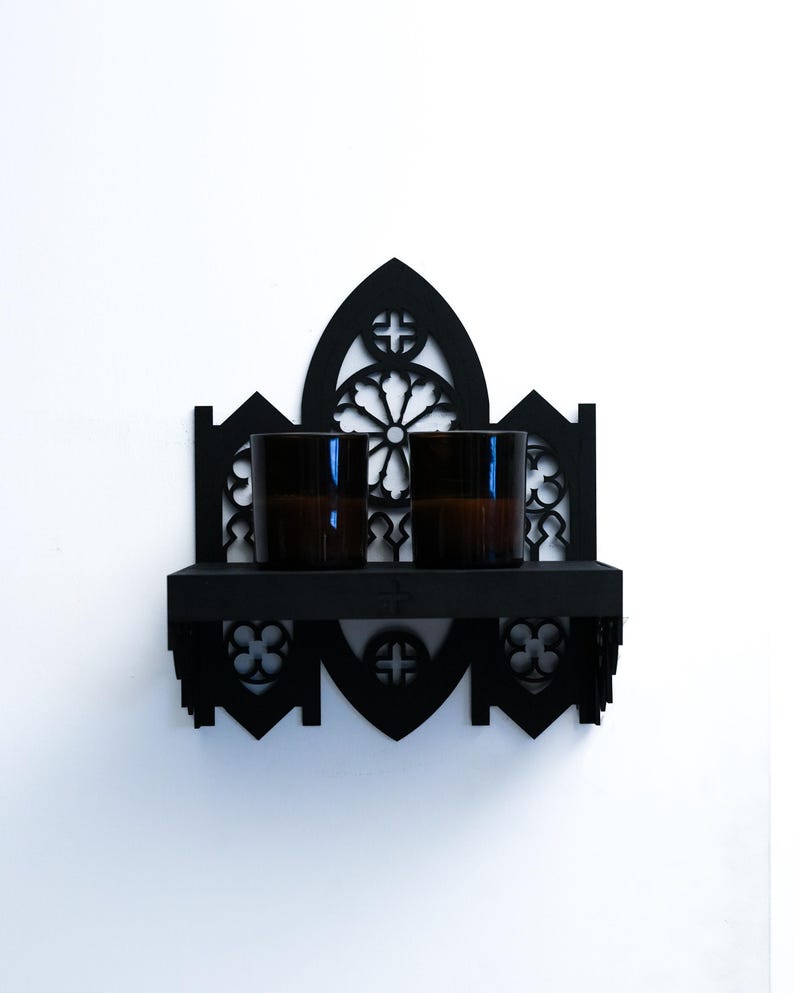 Peut inclure: Une &eacute;tag&egrave;re murale noire de style gothique, avec un sommet en arc et une petite &eacute;tag&egrave;re. Deux verres bruns sont pos&eacute;s sur l'&eacute;tag&egrave;re. Le design pr&eacute;sente des croix d&eacute;coup&eacute;es et des motifs floraux.