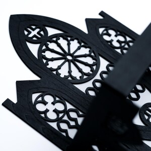 Peut inclure: Gros plan sur un panneau d&eacute;coratif en bois noir avec un motif de fen&ecirc;tre gothique. Le panneau pr&eacute;sente des motifs d&eacute;coup&eacute;s complexes, dont un motif circulaire central et des &eacute;l&eacute;ments en forme de croix. Le panneau est pos&eacute; sur un fond blanc.