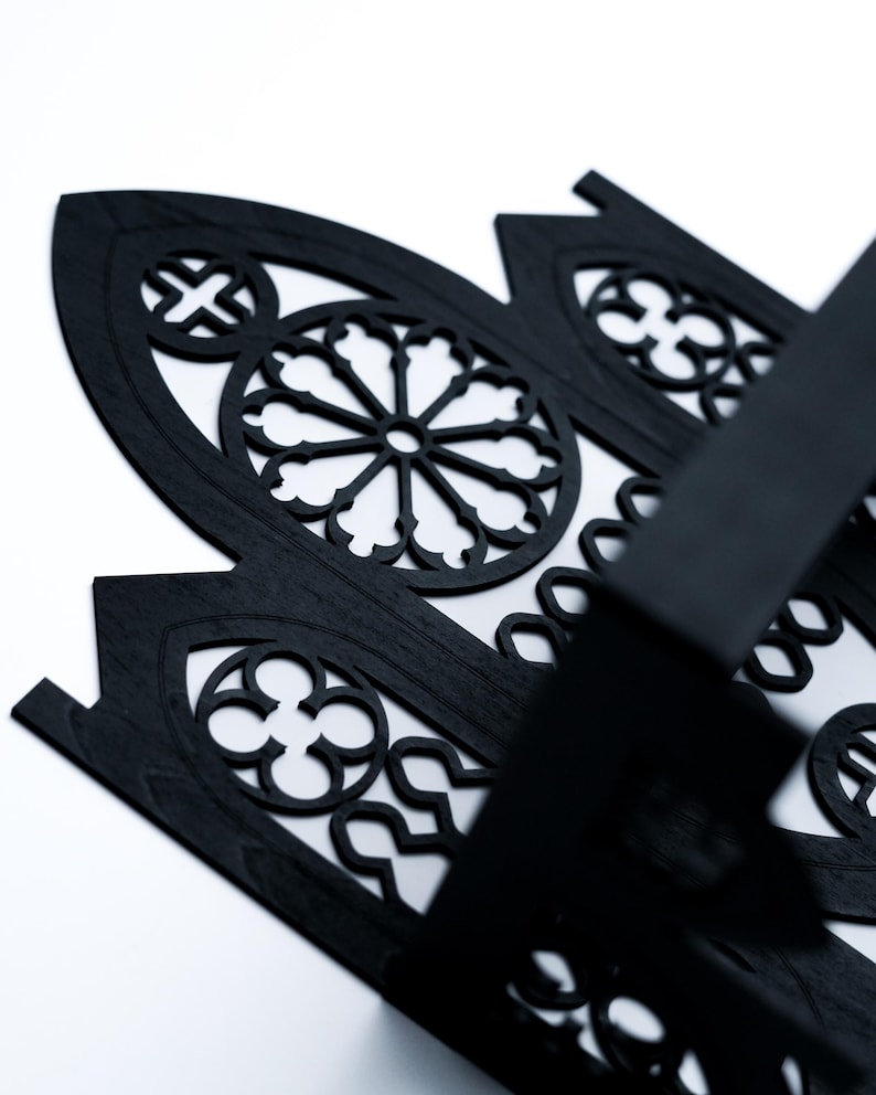 Peut inclure: Gros plan sur un panneau d&eacute;coratif en bois noir avec un motif de fen&ecirc;tre gothique. Le panneau pr&eacute;sente des motifs d&eacute;coup&eacute;s complexes, dont un motif circulaire central et des &eacute;l&eacute;ments en forme de croix. Le panneau est pos&eacute; sur un fond blanc.