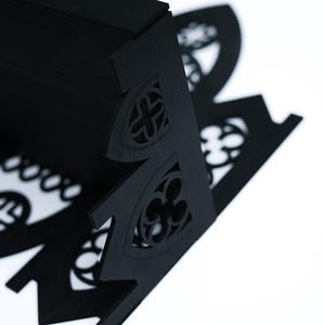 Peut inclure: &Eacute;tag&egrave;re d&eacute;corative noire d&eacute;coup&eacute;e au laser avec des d&eacute;tails architecturaux gothiques. L'&eacute;tag&egrave;re pr&eacute;sente des motifs d&eacute;coup&eacute;s complexes de croix et de quadrilobes. L'&eacute;tag&egrave;re est faite d'un mat&eacute;riau sombre et est pos&eacute;e sur un fond blanc.