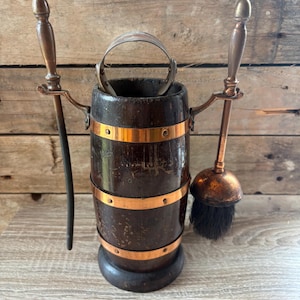 May include: A dark brown wooden bucket with three horizontal copper bands, a metal handle, and two side attachments holding a long metal poker and a round brush with dark bristles. The bucket features a cylindrical shape and a sturdy base.