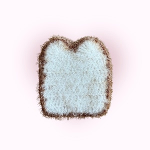 May include: A handmade, plush bread slice with a white centre and a brown, textured crust. The bread slice is made of soft, fluffy material and is set against a light pink background. This item is likely a decorative item or a toy.