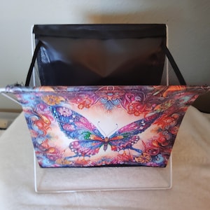 May include: A white metal wire frame with a black fabric liner and a colorful butterfly design. The fabric liner has a mesh opening at the top.