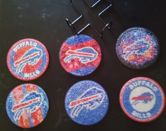 May include: Six round coasters featuring a Buffalo Bills logo. The coasters are made from a sparkly material and come in different colour combinations of blue, red, white and black.