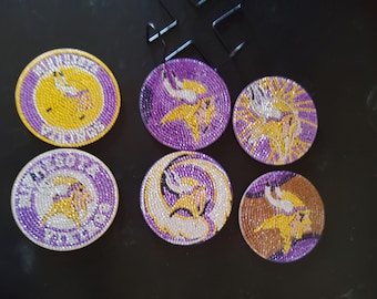 May include: Six purple and gold coasters with a Viking logo. The coasters are made of rhinestones and feature a different design on each one.
