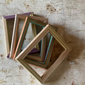 Könnte beinhalten: Fünf Bilderrahmen aus Holz, hergestellt aus recycelten Skateboards. Die Rahmen sind übereinander gelegt und haben verschiedene Farben, darunter Grün, Orange, Lila und Braun.