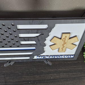 May include: A wooden American flag with a blue line and a Star of Life symbol. The flag is split in half, with the Star of Life on the right side. The text "Remarkable" is printed below the Star of Life.