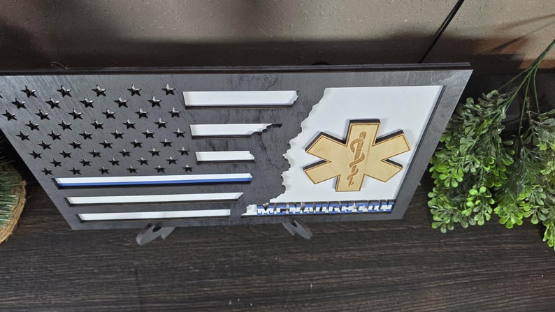 May include: A wooden American flag with a blue line and a Star of Life symbol. The flag is split in half, with the Star of Life on the right side. The text "Remarkable" is printed below the Star of Life.