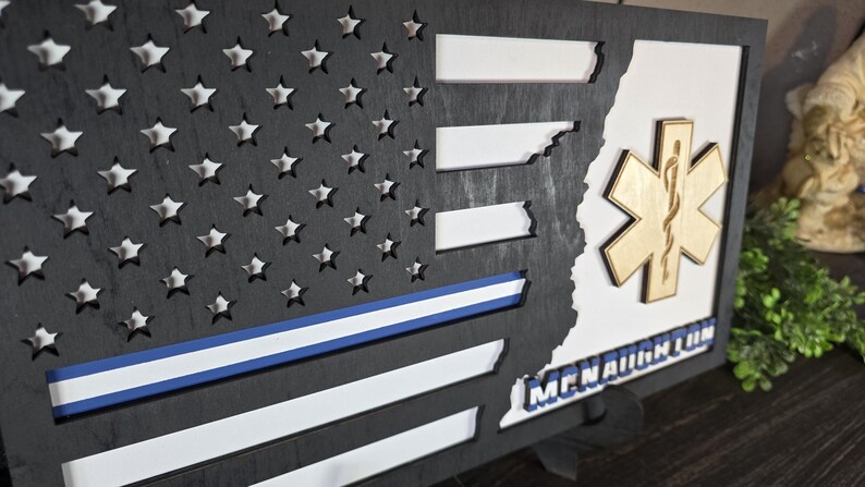 May include: A wooden American flag with a blue line, a gold star of life, and the text "McNaughton" on a white background.