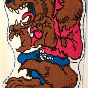 May include: A brown werewolf with a pink shirt and blue jeans is snarling with its mouth open and tongue sticking out. The werewolf has green eyes and sharp teeth. The image is on a white background with a blue dotted border.