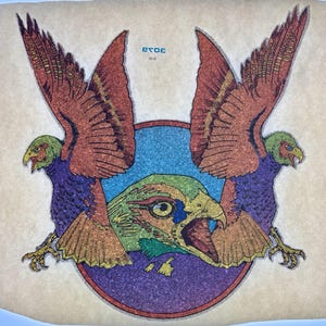 May include: A temporary tattoo sheet featuring two symmetrical birds with orange wings, purple bodies, and green heads flanking a central green bird head. The design includes a blue circular background and the text 3079 printed in blue.