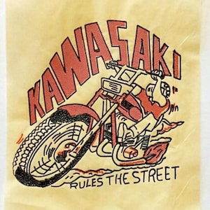 May include: A vintage iron-on patch featuring a red Kawasaki motorcycle with the text "Kawasaki! Rules the Street". The patch is on a yellow background with instructions for applying the patch to fabric.