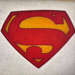 May include: The iconic Superman logo, a red diamond shape with a yellow 'S' in the center, outlined in black. The image is set against a white background, showcasing the bold colors and design of the superhero emblem.
