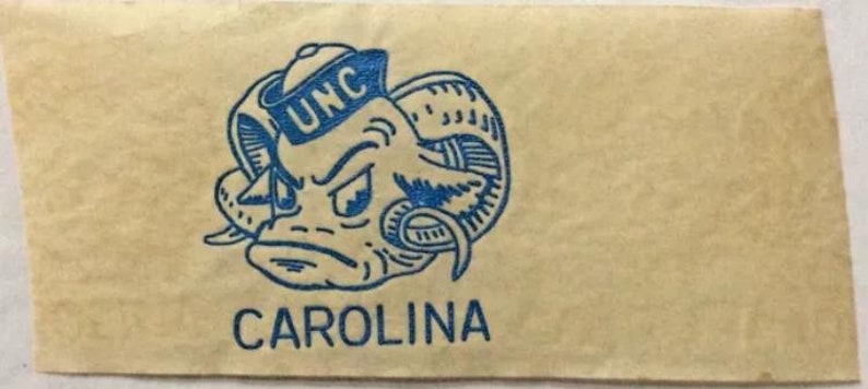 May include: A blue and white mascot logo with the text "UNC" and "CAROLINA" on a light brown background.