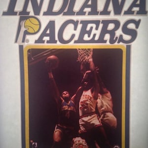 May include: A vintage Indiana Pacers basketball poster featuring two players in action. The poster has a blue and yellow color scheme with the team's logo at the top. The text "QUAKER 78" is at the bottom of the poster.