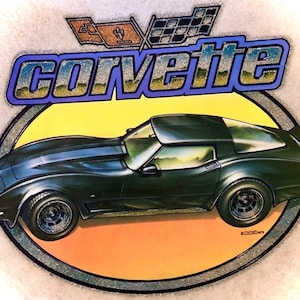 May include: A graphic iron-on transfer featuring a black Corvette sports car centered on a yellow and orange oval background. Above the car, the word CORVETTE is written in blue letters with a glittery finish, topped by the Chevrolet logo.