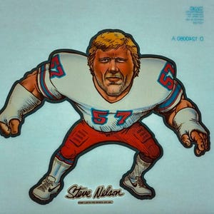 May include: A cartoon illustration of a football player wearing a white jersey with blue and red accents. The jersey has the number "57" on the front. The player is wearing red pants and white shoes. The player's name, "Steve Nelson", is written below the image.