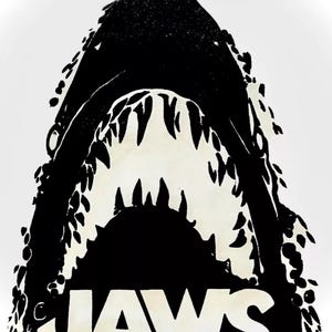 May include: Black and white illustration of a shark's open mouth with sharp teeth. The word "JAWS" is printed below the shark's mouth.