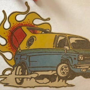 May include: A cartoon illustration of a vintage van with a yellow top and blue body, set against a backdrop of stylized flames. The van is depicted with large wheels and a retro design, evoking a sense of adventure.