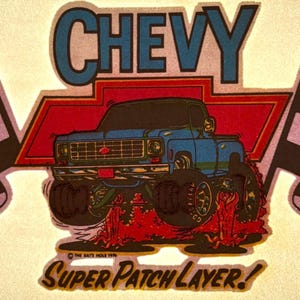 May include: A vintage-style graphic featuring a blue Chevy truck with large tires, set against a red and white background. The word "CHEVY" is at the top, with "SUPER PATCH LAYER!" at the bottom, and checkered flags on either side.
