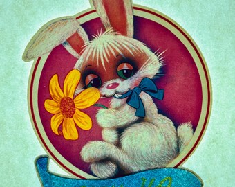 May include: A white rabbit with pink ears holds a yellow flower and wears a blue bow. The rabbit is inside a red circle with a white border. The text "LUV YA" is on a blue banner.