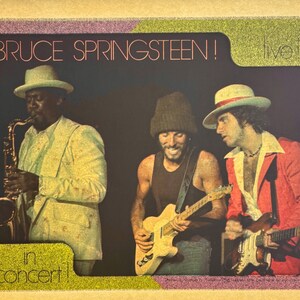 May include: Vintage concert poster featuring Bruce Springsteen and band members. The poster has a retro design with the text "BRUCE SPRINGSTEEN! live!" and "in concert!" The image shows musicians playing instruments, including a saxophone and guitars.