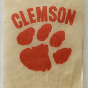 May include: A white paper bag with the word "CLEMSON" printed in orange letters and an orange paw print.