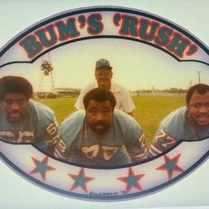 May include: A vintage sticker featuring a football team called "Bum's Rush". The sticker is oval-shaped with a blue and white color scheme. It features three football players in blue and white uniforms, with a coach standing behind them. The sticker has a white background with three blue stars.