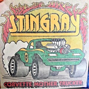 May include: A graphic print featuring a green hot rod car with large tires and an exposed engine. The word STINGRAY is in yellow letters at the top, surrounded by red flames. The text CORVETTE MOTHER TRUCKER is printed in red at the bottom.
