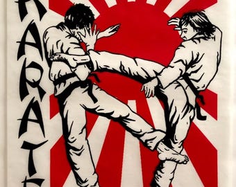 Puede incluir: Ilustración en blanco y negro de dos karatecas en acción, con un sol naciente rojo y blanco detrás de ellos. La palabra "KARATE" está escrita verticalmente en el lado izquierdo de la imagen.