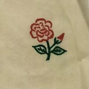 May include: A simple hand-drawn illustration of a red rose with green leaves and stem on a cream-colored background.