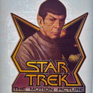 May include: A vintage Star Trek The Motion Picture iron-on transfer featuring a portrait of Spock centered within a large, gold-outlined star shape. The text Star Trek The Motion Picture is printed in black at the bottom with copyright details.