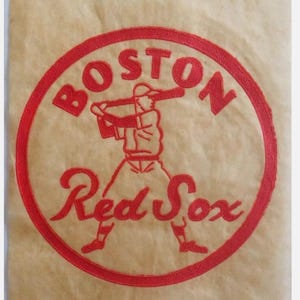 May include: A red circle with the words "Boston Red Sox" in a white cursive font. Inside the circle is a red silhouette of a baseball player swinging a bat.
