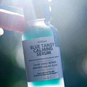 K&ouml;nnte beinhalten: Eine klare Glasflasche mit AliBee Blue Tansy Calming Serum und einem wei&szlig;en Etikett. Der Text auf dem Etikett lautet: AliBee BLUE TANSY CALMING SERUM with sea buckthorn & carrot seed oil, CALMS VISIBLE REDNESS, RESTORES HEALTHY GLOW, formulated for skin in perimenopause & beyond, 1 oz : 30 ml.