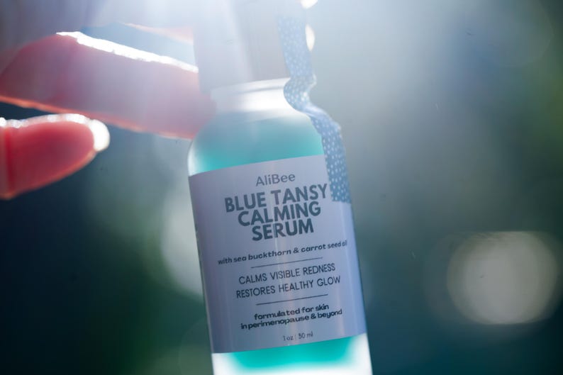 K&ouml;nnte beinhalten: Eine klare Glasflasche mit AliBee Blue Tansy Calming Serum und einem wei&szlig;en Etikett. Der Text auf dem Etikett lautet: AliBee BLUE TANSY CALMING SERUM with sea buckthorn & carrot seed oil, CALMS VISIBLE REDNESS, RESTORES HEALTHY GLOW, formulated for skin in perimenopause & beyond, 1 oz : 30 ml.