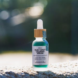K&ouml;nnte beinhalten: Eine Glasflasche mit Pipette, die ein blaugr&uuml;nes Blue Tansy Calming Serum enth&auml;lt, mit einem Bambusring und wei&szlig;em Pipettenaufsatz. Das Etikett tr&auml;gt die Aufschrift AliBee BLUE TANSY CALMING SERUM, calms visible redness, restores healthy glow, 1 oz / 30 ml.