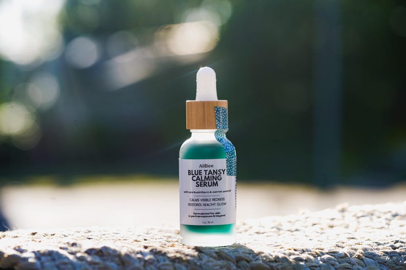 K&ouml;nnte beinhalten: Eine Glasflasche mit Pipette, die ein blaugr&uuml;nes Blue Tansy Calming Serum enth&auml;lt, mit einem Bambusring und wei&szlig;em Pipettenaufsatz. Das Etikett tr&auml;gt die Aufschrift AliBee BLUE TANSY CALMING SERUM, calms visible redness, restores healthy glow, 1 oz / 30 ml.