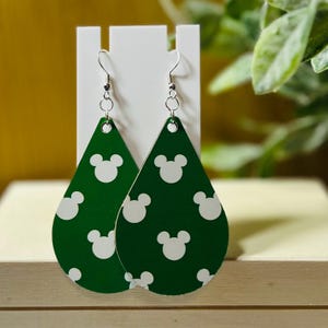Puede incluir: Pendientes verdes en forma de l&aacute;grima con un estampado blanco de Mickey Mouse. Los pendientes tienen ganchos para las orejas de color plateado. Los pendientes se exhiben en un soporte blanco.